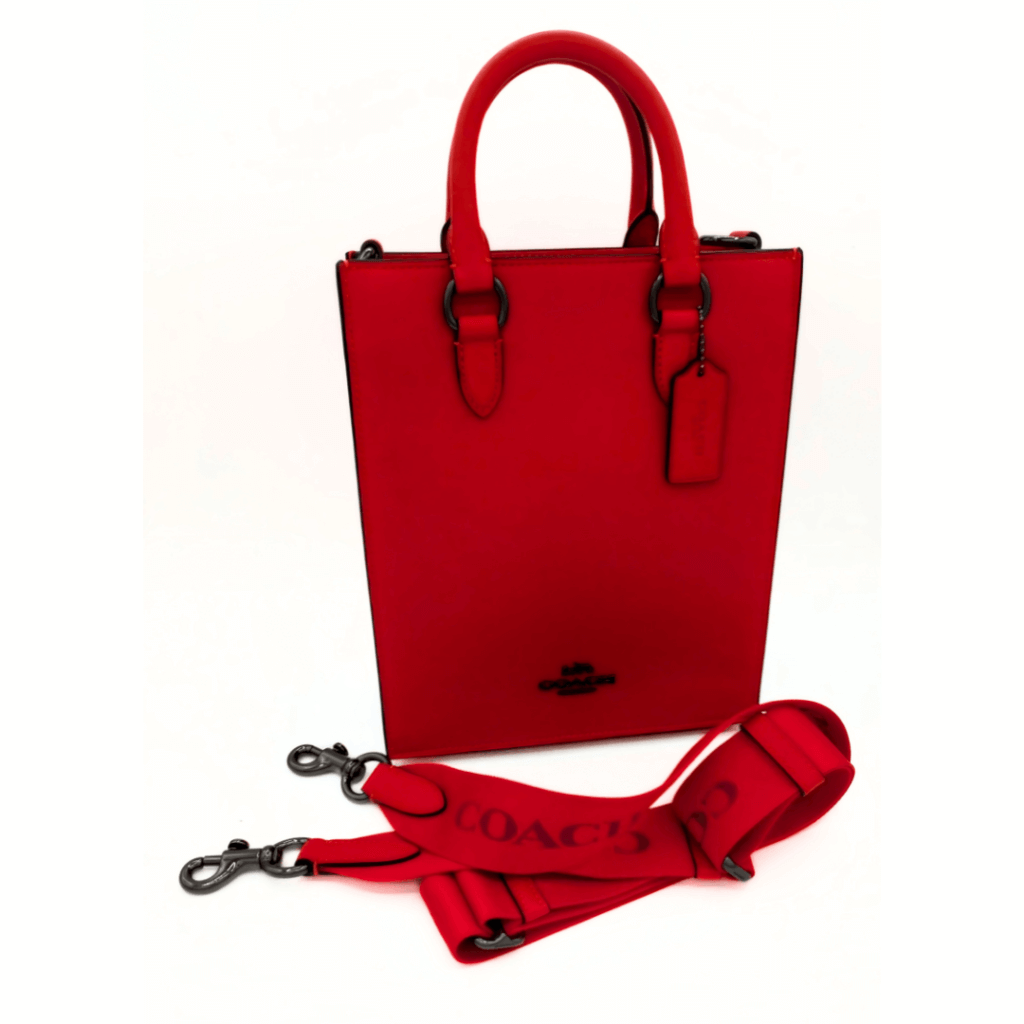 A striking red Coach Dylan bag with structured handles and a detachable matching shoulder strap, displayed against a white background, emphasizing its bold color and contemporary design.