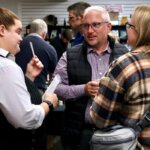 A young woman dressed as a reporter engaging in a conversation with two adults at the Murder Mystery event. They appear to be discussing or sharing information in a lively social setting.