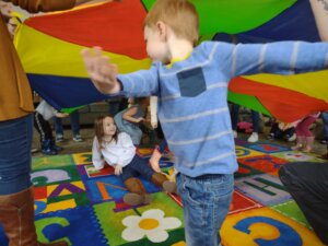 Children play under a colorful parachute during a group activity on a vibrant alphabet rug, laughing and enjoying the moment.