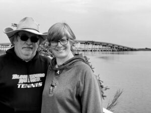 Marty and Lisa Coyne in a black and white photo with a bridge in the background. They are smiling.