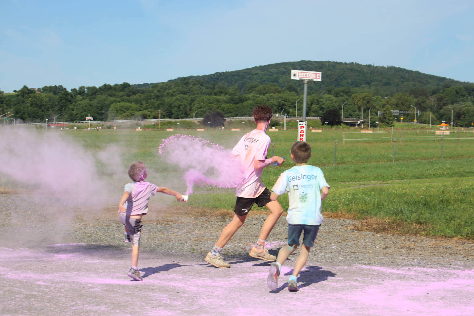 Two smaller boys throw purple powder at an older boy. All three are running away from the camera.