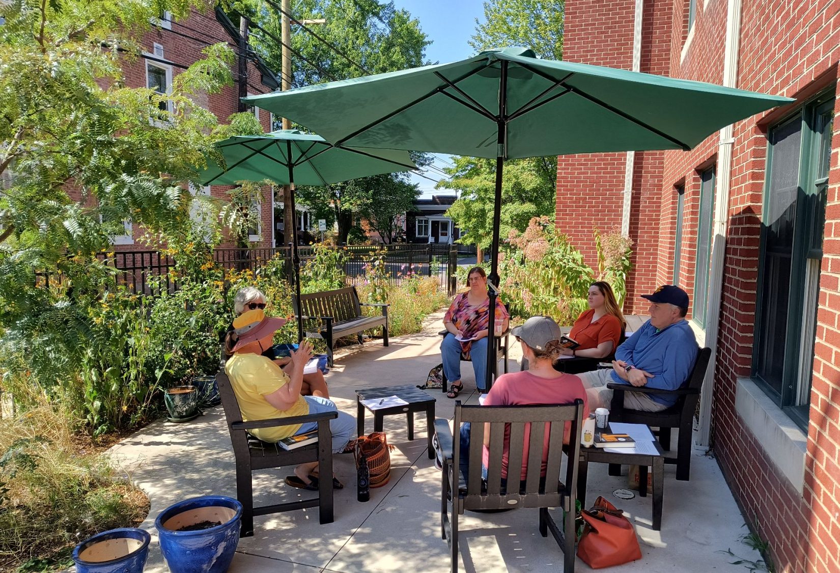 A book club meets under the patio umbrellas in the colorful garden.